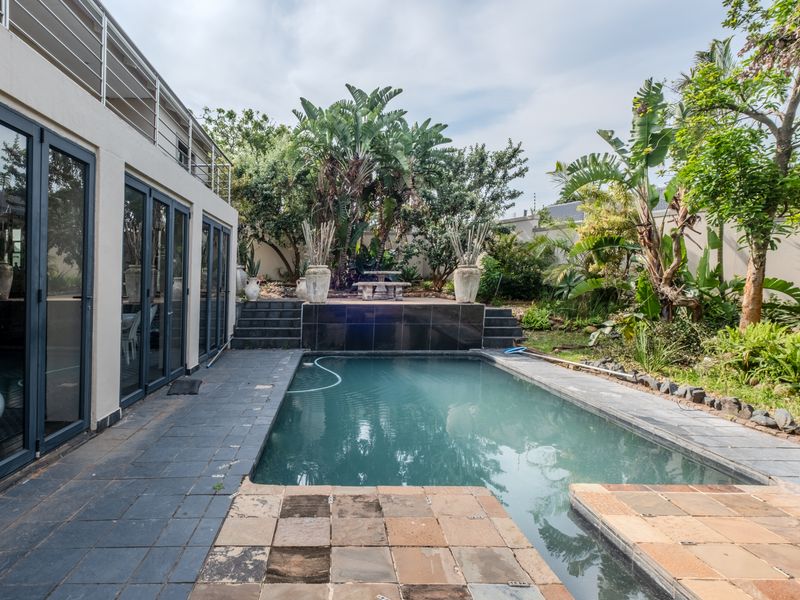 Outdoor pool area featuring a tiled surround, raised stone patio with steps, and direct access to the home through large bi-fold glass doors.