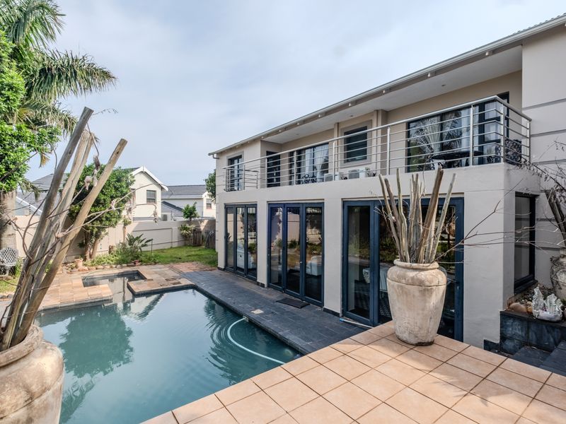 Rear view of a two-story home featuring a swimming pool, tiled patio area, and an upper-level balcony with stainless steel railings.
