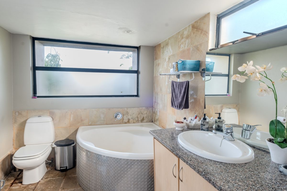 A functional bathroom featuring a corner bathtub with metal-look paneling, a granite-topped vanity with a drop-in sink, and neutral stone-style wall tiling.
