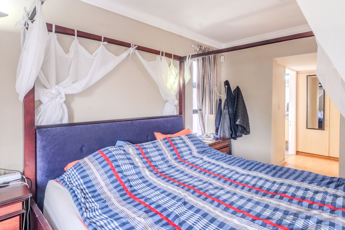 A comfortable bedroom featuring laminate flooring, built-in cupboards, and decorative cornice detailing, offering a functional and well-proportioned living space.