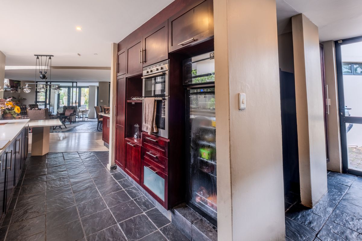 A spacious kitchen featuring dark wood cabinetry, built-in oven, integrated wine cooler, and durable slate tile flooring, flowing into an open-plan living area.