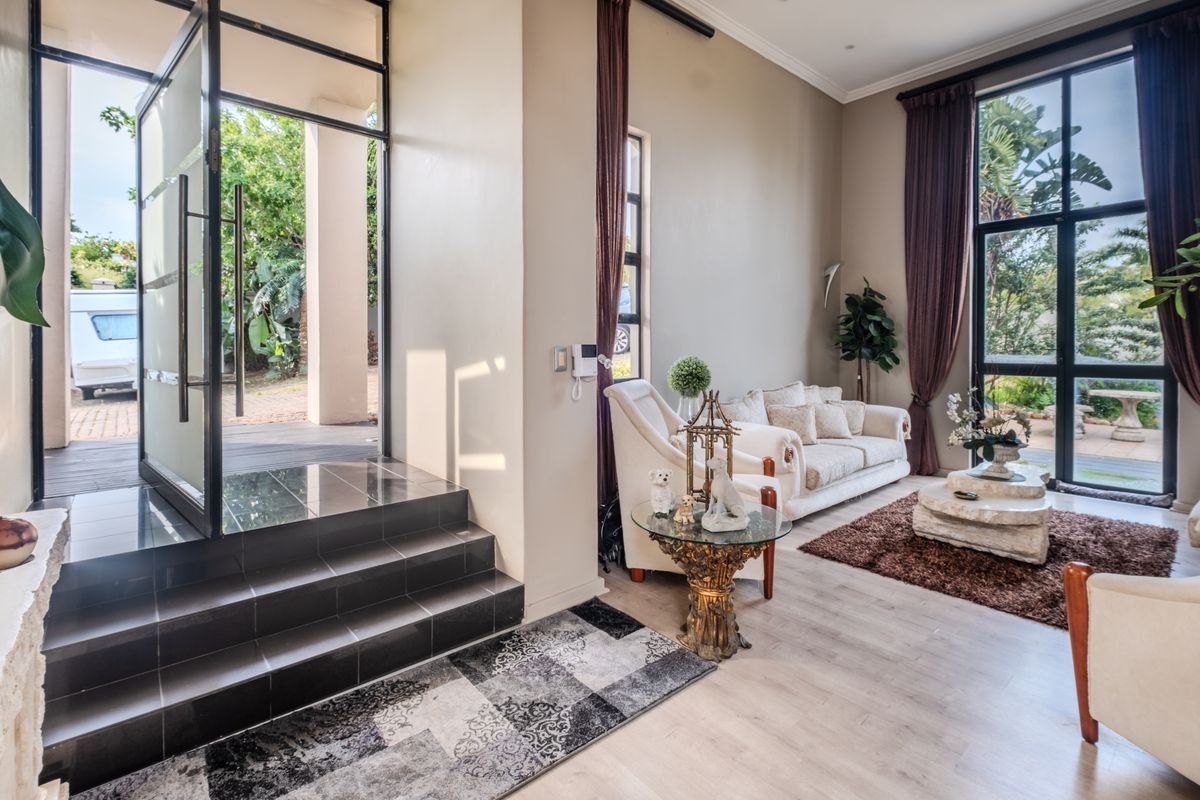 Bright living room featuring high ceilings, large floor-to-ceiling windows, and a modern black metal-framed glass entrance door with tiled steps.