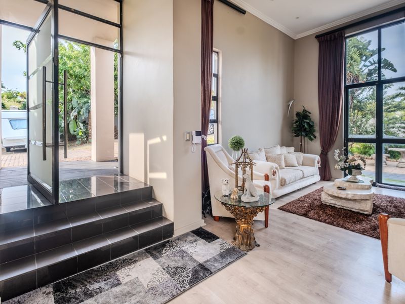 Bright living room featuring high ceilings, large floor-to-ceiling windows, and a modern black metal-framed glass entrance door with tiled steps.