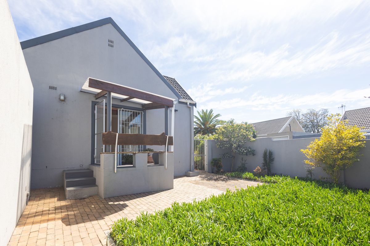 Rear exterior view featuring a paved patio area, timber pergola, and a private garden enclosed by boundary walls.