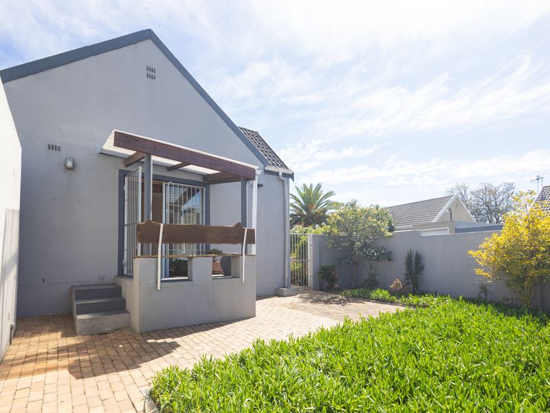 Rear exterior view featuring a paved patio area, timber pergola, and a private garden enclosed by boundary walls.