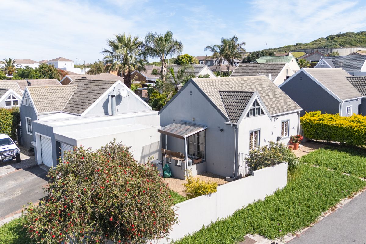 An aerial view of a residential property featuring a tiled roof, paved driveway, garage, and a small covered patio area within a suburban estate.