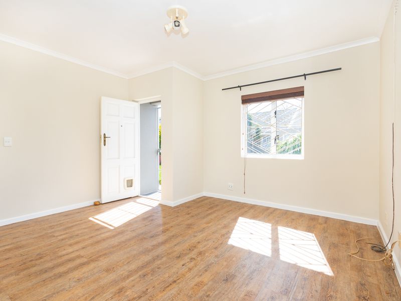 A bright, empty living room featuring laminate flooring, a window with security bars, and a direct exterior access door.