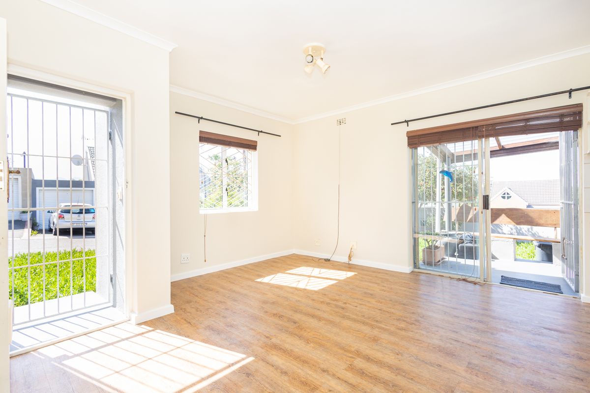 Bright and spacious living area featuring wood-look laminate flooring, large sliding glass doors with security gates, and neutral wall finishes.