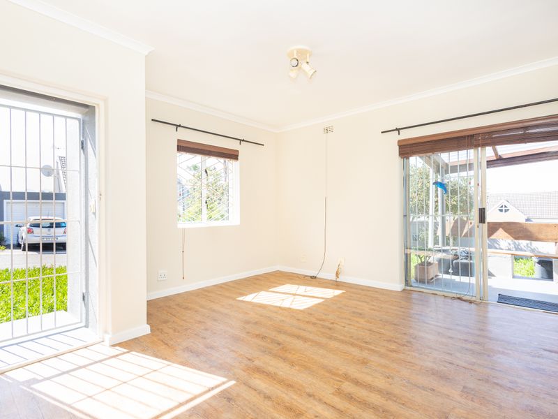 Bright and spacious living area featuring wood-look laminate flooring, large sliding glass doors with security gates, and neutral wall finishes.