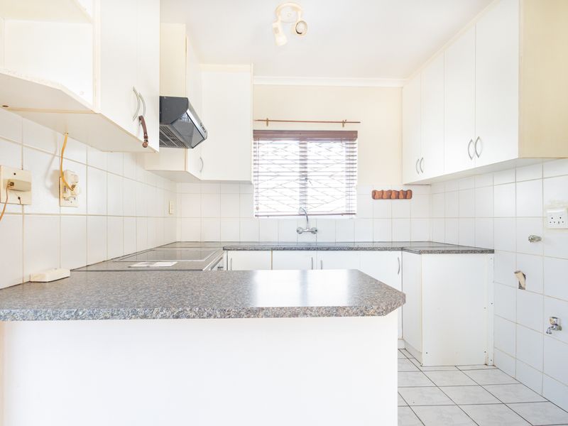 A functional kitchen featuring white cabinetry, laminate countertops, and tiled finishes. The space is vacant and ready for modernization or cosmetic updates.