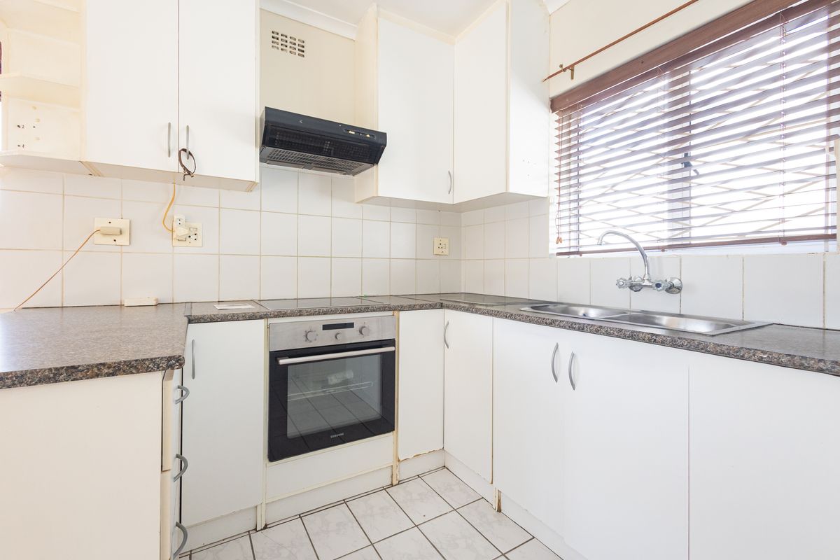 A functional kitchen featuring built-in cabinetry, an oven, hob, extractor fan, and a double sink with tiled backsplash and flooring.