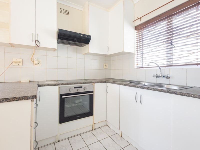A functional kitchen featuring built-in cabinetry, an oven, hob, extractor fan, and a double sink with tiled backsplash and flooring.