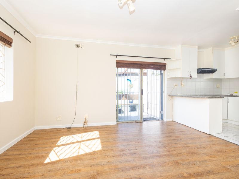 An open-plan living and kitchen area featuring laminate flooring, white cabinetry, and direct access to an outdoor space through a sliding security door.