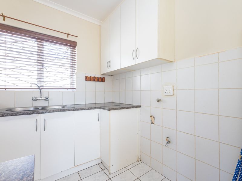Functional laundry room featuring built-in white cabinetry, tiled splashback, stainless steel sink, and dedicated plumbing connections for laundry appliances.