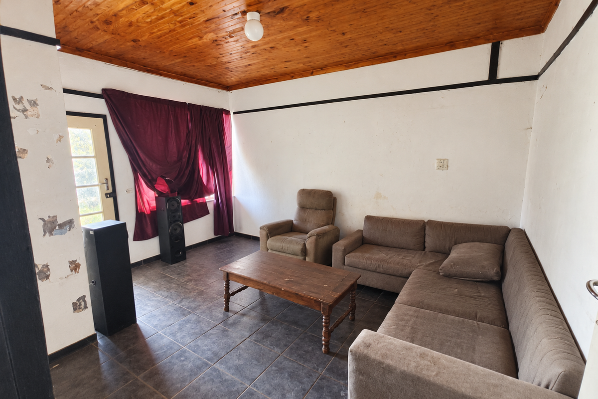 A living room featuring a timber tongue and groove ceiling, dark ceramic floor tiles, and a glass panel door leading to the exterior.