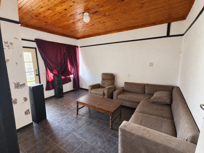 A living room featuring a timber tongue and groove ceiling, dark ceramic floor tiles, and a glass panel door leading to the exterior.