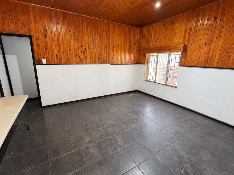 An empty living room featuring dark tiled flooring and distinctive wooden wall paneling, offering a blank canvas for renovation and interior design updates.