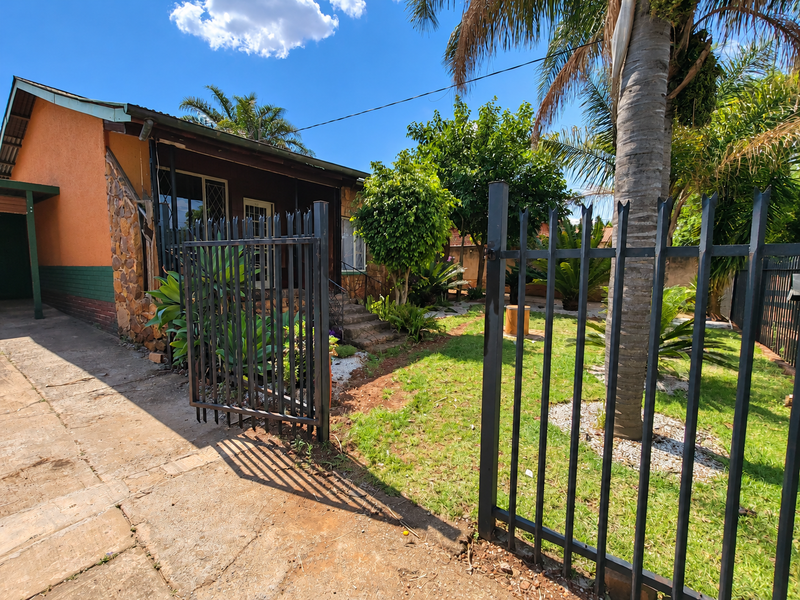 Front view of the property featuring a metal security gate, concrete driveway, and stone-clad exterior wall with a covered porch entrance.