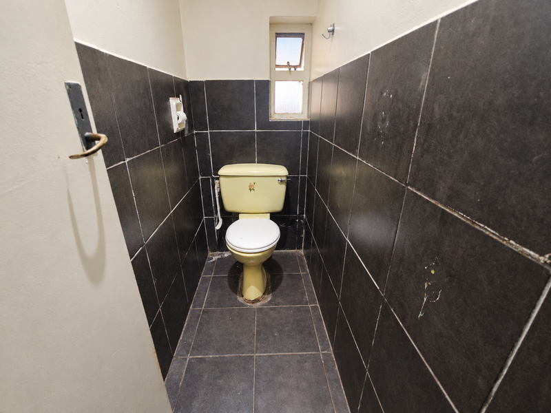 A compact bathroom featuring dark wall and floor tiles, a window for ventilation, and a standard toilet.