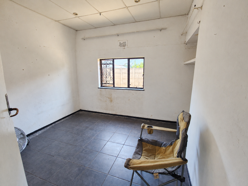 A vacant bedroom featuring dark tiled flooring, a drop ceiling, and security bars on the window, requiring cosmetic updates to improve its overall condition.
