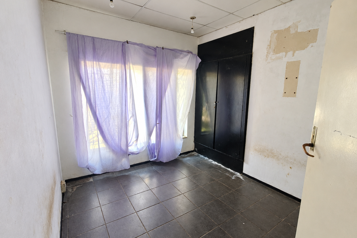 An empty bedroom featuring dark tiled flooring, a built-in cupboard, and a drop ceiling, requiring cosmetic renovation and wall repairs.