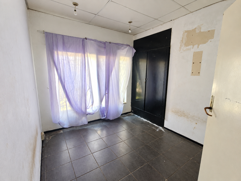 An empty bedroom featuring dark tiled flooring, a built-in cupboard, and a drop ceiling, requiring cosmetic renovation and wall repairs.