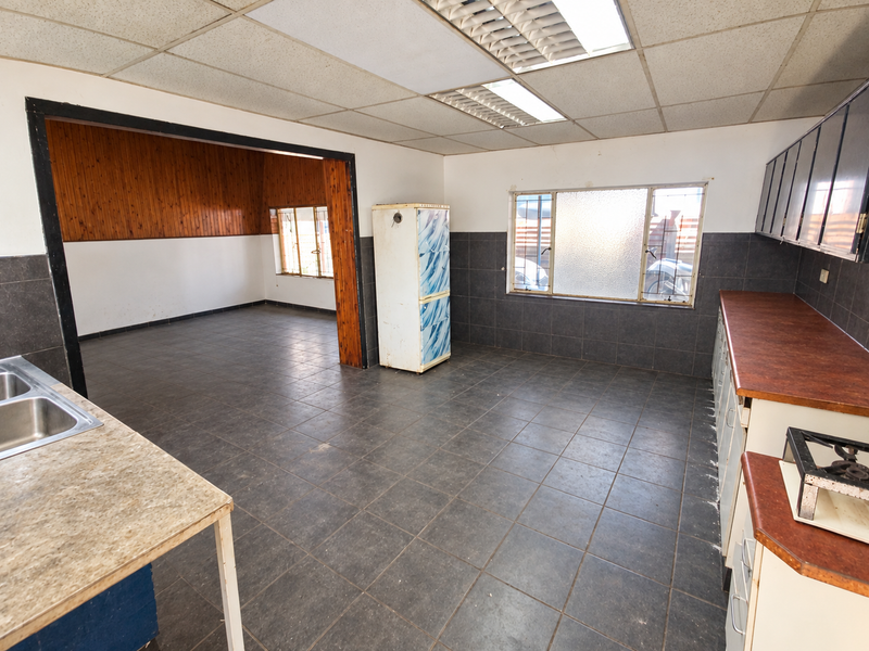 Spacious kitchen area featuring dark tiled flooring, built-in cabinetry with laminate countertops, and a drop ceiling, offering significant potential for modernization.