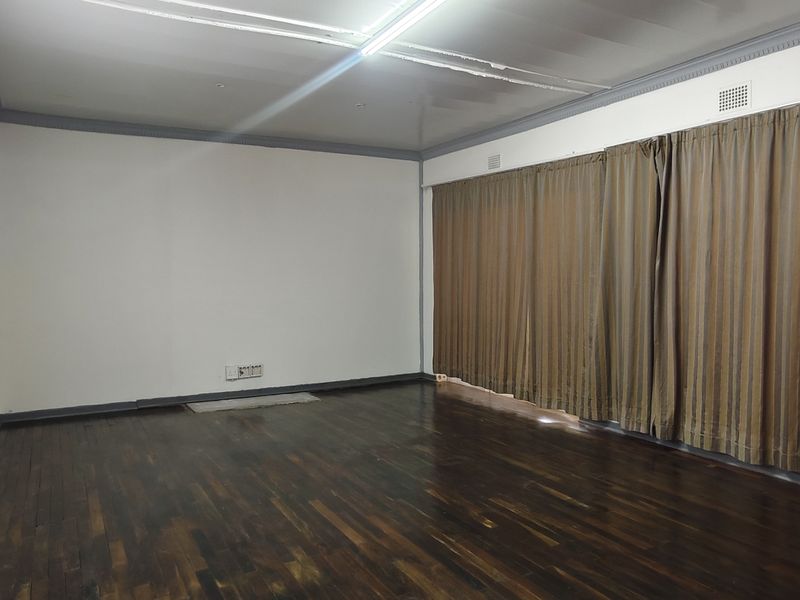 Spacious living room featuring dark parquet flooring, crown molding, and large windows with curtains, offering a blank canvas for interior design.
