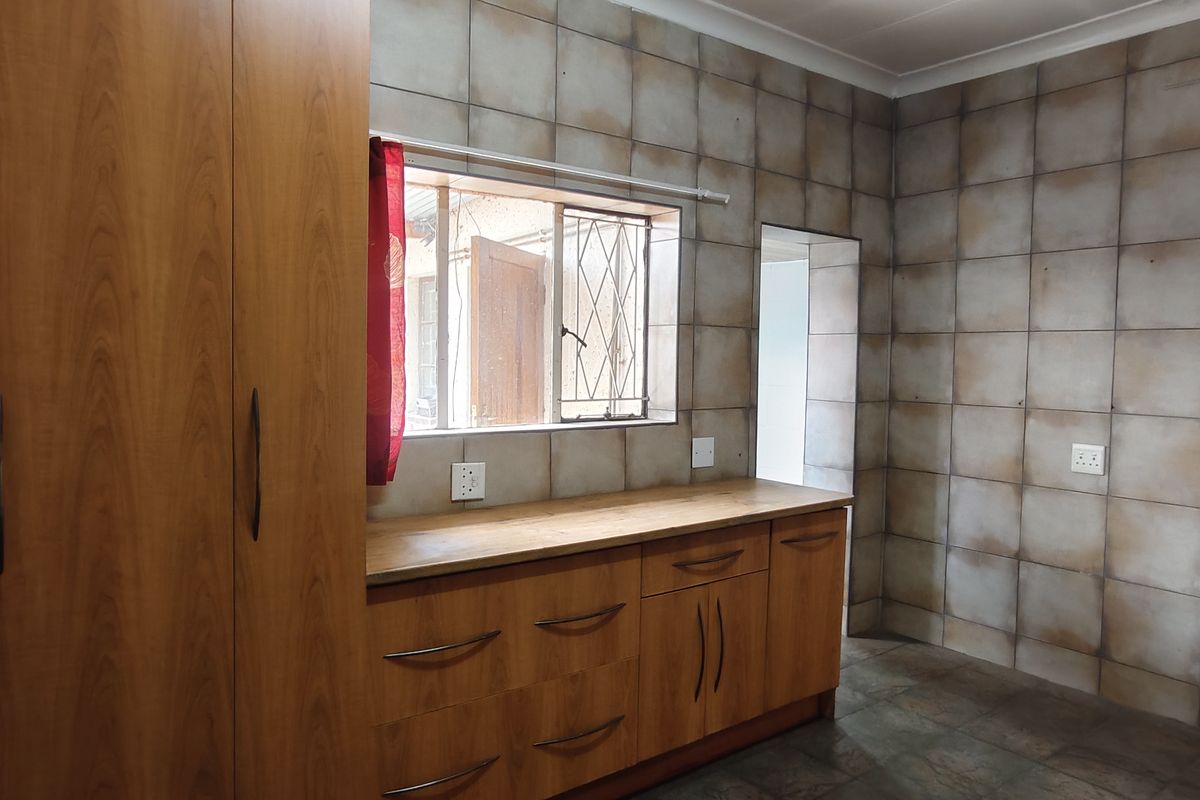 A functional kitchen space featuring built-in wooden cabinetry, laminate countertops, and full-height wall tiling, offering a clean and practical layout.