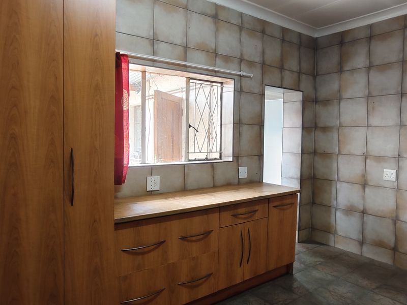 A functional kitchen space featuring built-in wooden cabinetry, laminate countertops, and full-height wall tiling, offering a clean and practical layout.