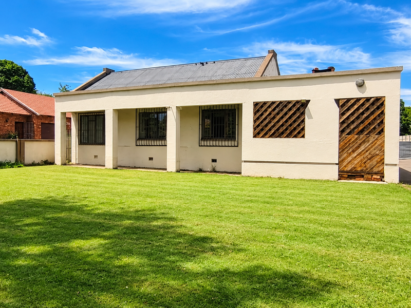 Rear view of the property featuring a covered patio, a spacious lawn, and a paved driveway enclosed by a precast concrete boundary wall.