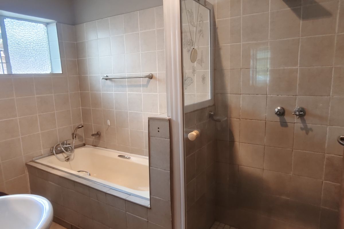 A functional bathroom featuring a built-in bathtub, separate shower enclosure, and toilet, finished with neutral wall tiles and an obscured glass window.