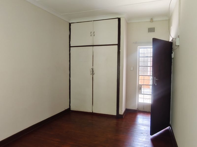 An empty bedroom featuring wooden flooring, built-in cupboards, and direct access to an exterior area through a security gate.