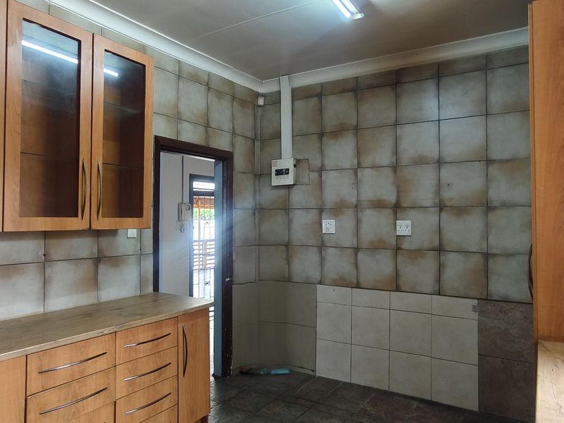 A functional kitchen space featuring built-in wooden cabinetry, laminate countertops, and tiled wall finishes, requiring cosmetic updates to improve the overall aesthetic.