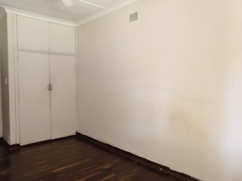 An empty bedroom featuring original timber flooring, built-in cupboards, and neutral wall finishes, offering a blank canvas for renovation or interior design.