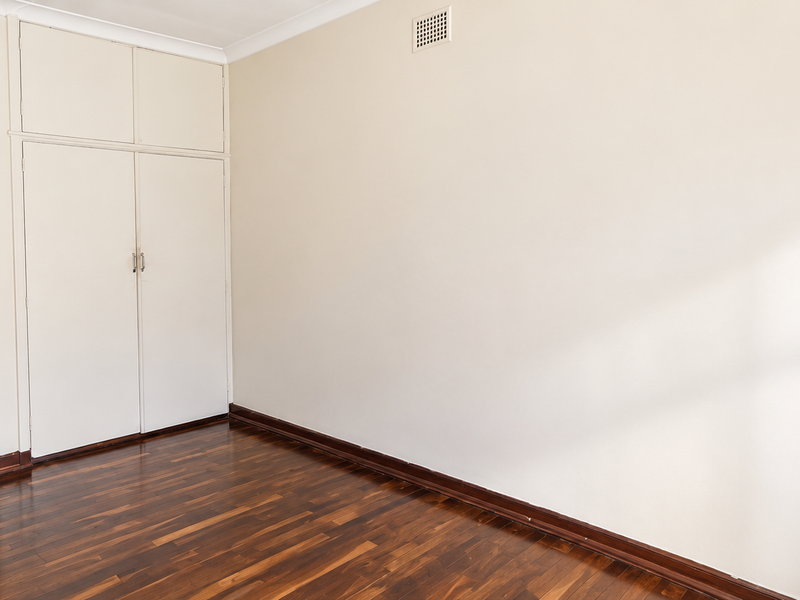 A bright, empty bedroom featuring polished timber flooring, built-in storage cabinetry, and neutral wall finishes.