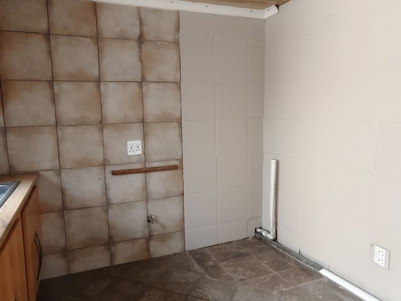 A functional scullery or utility area featuring a double bowl sink, built-in cabinetry, and tiled wall finishes, ready for renovation or modernization.