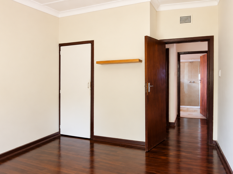 An empty bedroom featuring polished wooden flooring, a built-in cupboard, and direct access to an adjoining bathroom.