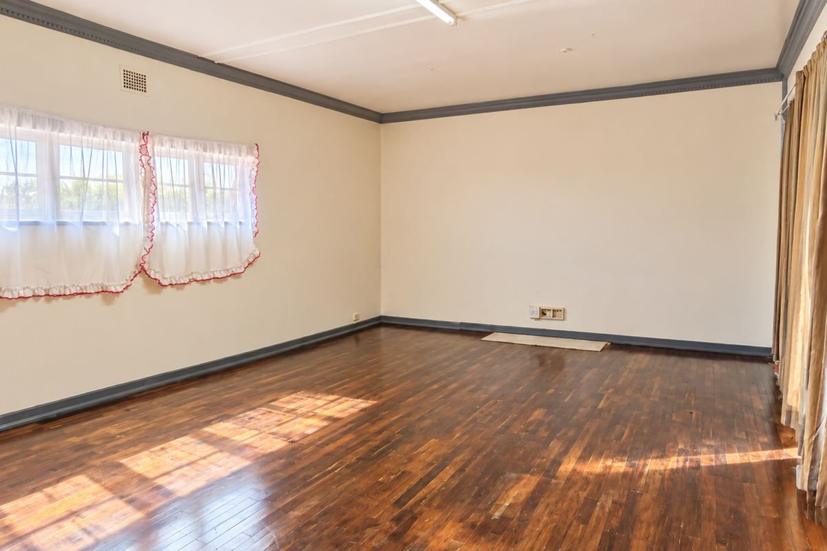 A spacious, empty living room featuring polished hardwood flooring, crown molding, and neutral wall tones, offering a blank canvas for interior design.