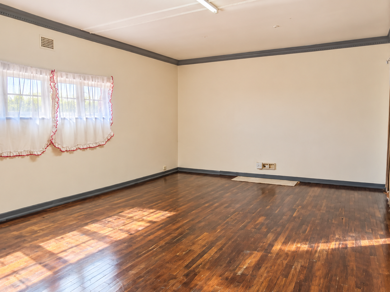 A spacious, empty living room featuring polished hardwood flooring, crown molding, and neutral wall tones, offering a blank canvas for interior design.