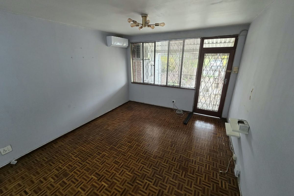 An empty living room featuring parquet flooring, a wall-mounted air conditioning unit, and a secure entrance door with security bars.