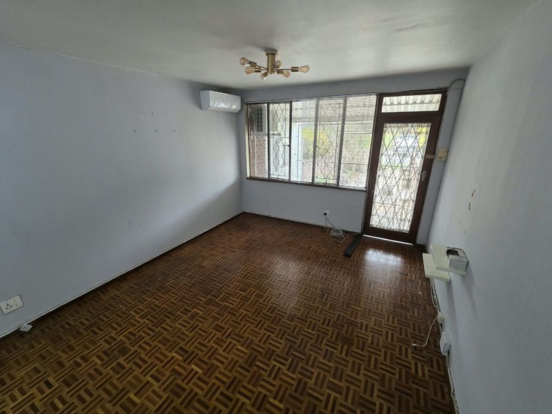 An empty living room featuring parquet flooring, a wall-mounted air conditioning unit, and a secure entrance door with security bars.