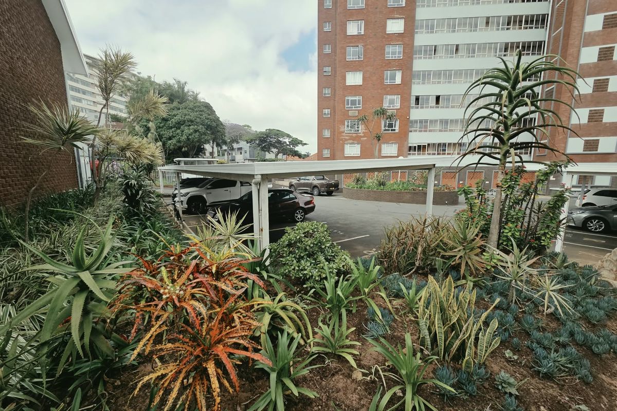 A view of the property's rear exterior featuring a landscaped garden with established plants and a covered carport area for vehicle parking.