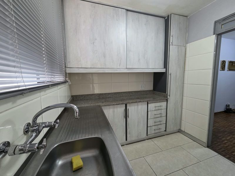 A functional kitchen featuring laminate cabinetry, granite countertops, a stainless steel sink, and tiled flooring, offering a clean and practical workspace.