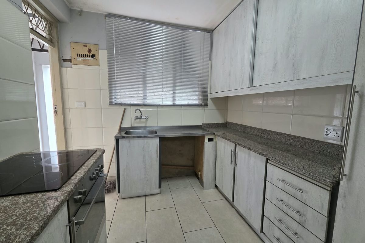 A functional kitchen featuring granite countertops, built-in cabinetry, and an integrated electric oven and hob, requiring minor repairs to cabinetry and ceiling finishes.