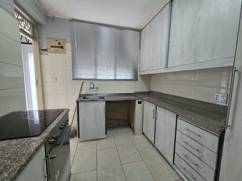 A functional kitchen featuring granite countertops, built-in cabinetry, and an integrated electric oven and hob, requiring minor repairs to cabinetry and ceiling finishes.