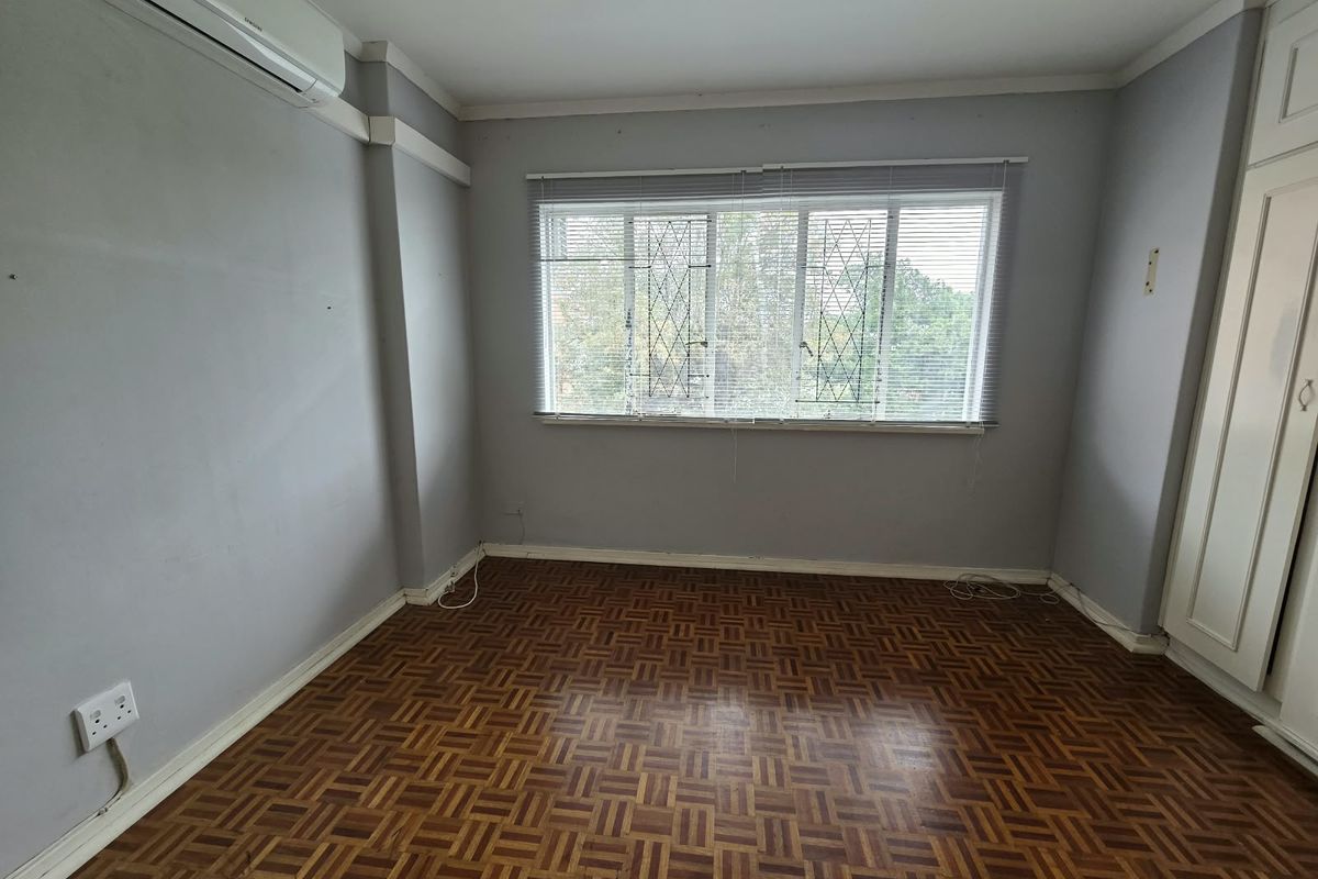 An empty bedroom featuring classic parquet flooring, built-in cupboards, and an installed air conditioning unit, offering a blank canvas for personalization.