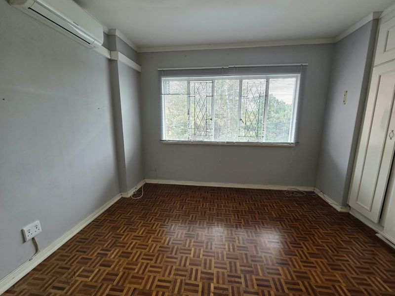 An empty bedroom featuring classic parquet flooring, built-in cupboards, and an installed air conditioning unit, offering a blank canvas for personalization.