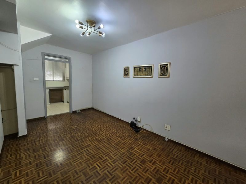 An empty living room featuring classic parquet flooring, a modern ceiling light fixture, and a direct doorway leading into the kitchen area.