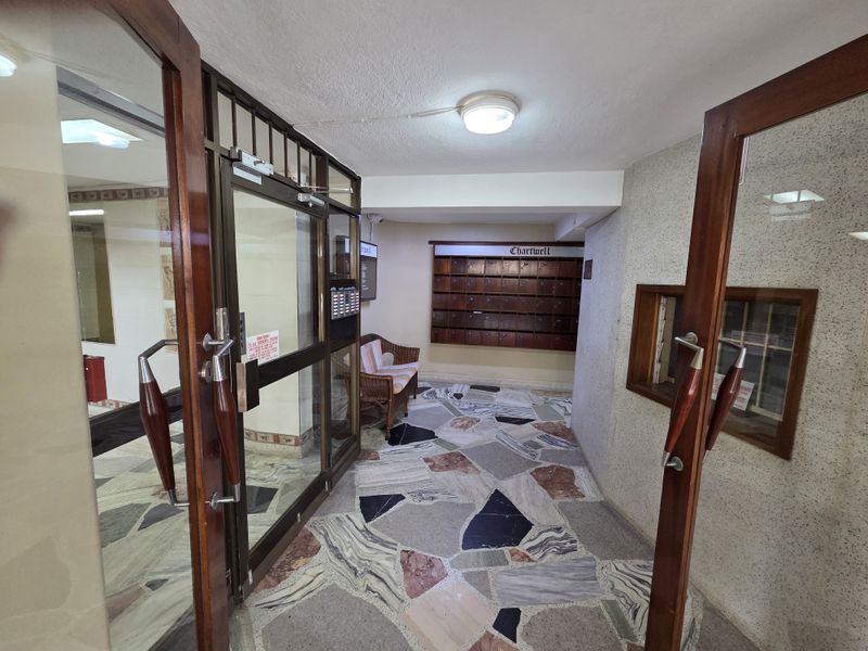 A secure building entrance lobby featuring terrazzo flooring, wooden framed glass doors, and a wall-mounted bank of mailboxes for residents.